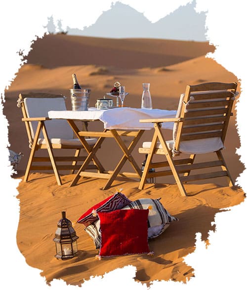 A luxury dining setup with chairs and table on the golden sand dunes of Morocco’s Sahara Desert
