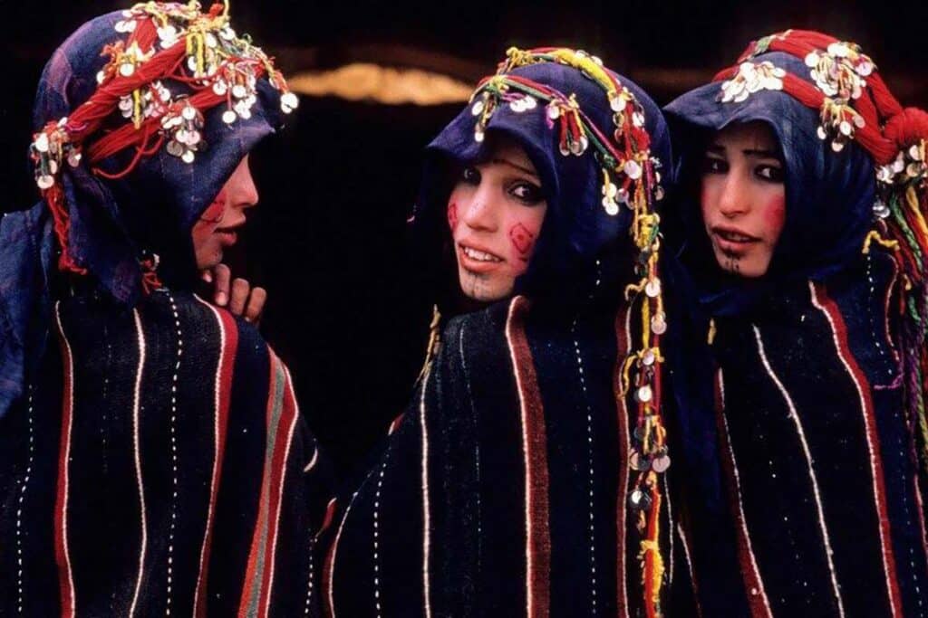 Three Amazigh women in traditional striped cloaks with coin-adorned headscarves