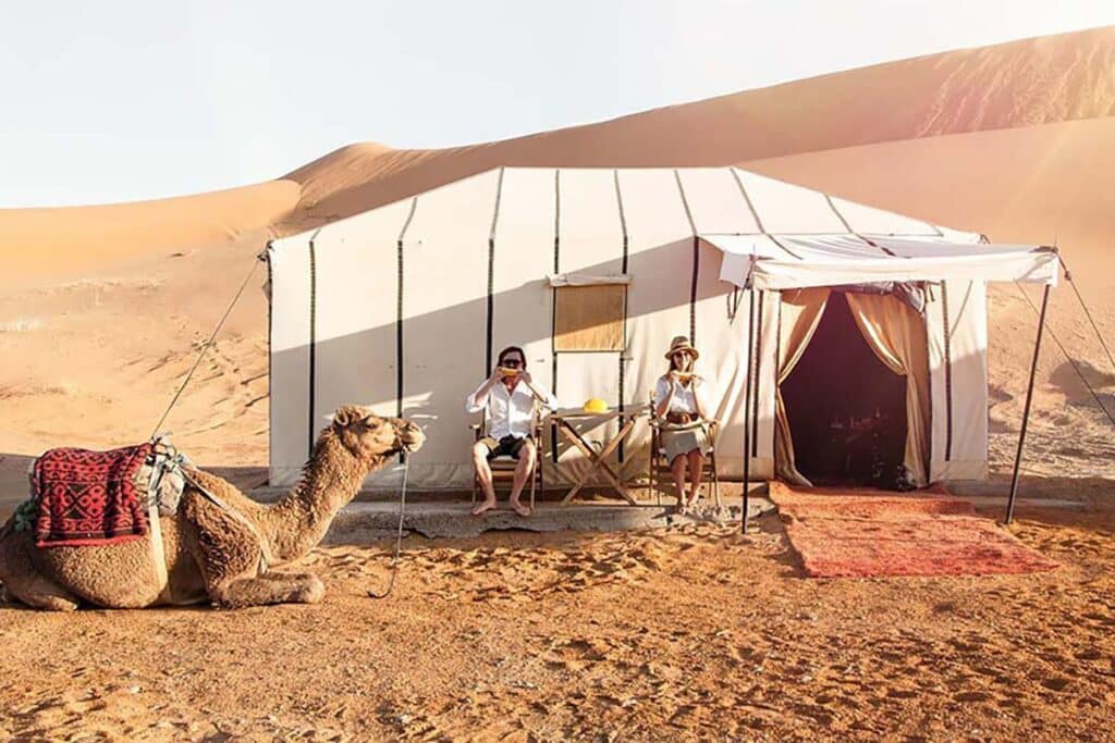 Luxury desert tent in Erg Chebbi with seated travellers & resting camel