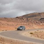 Silver rental car winding along a deserted Atlas Mountain road under dramatic skies.