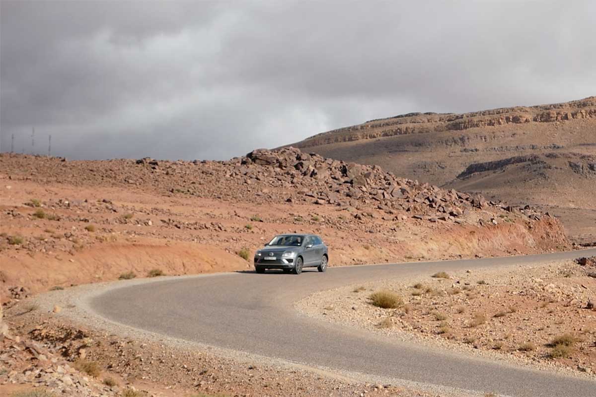 Silver rental car winding along a deserted Atlas Mountain road under dramatic skies.