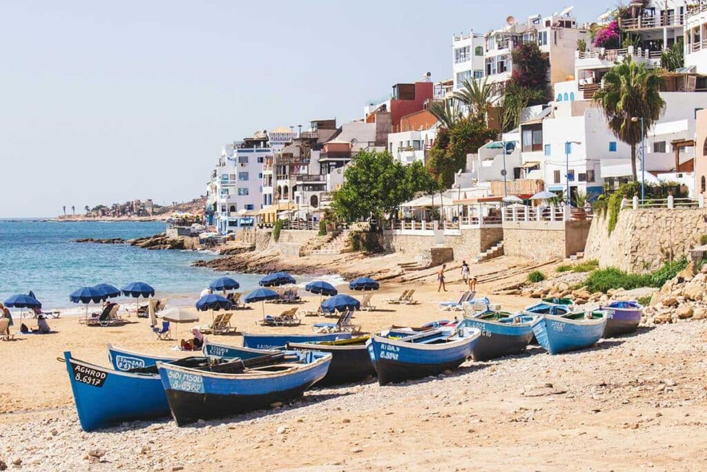 Sandy beach with umbrellas and blue fishing boats in Taghazout near Agadir
